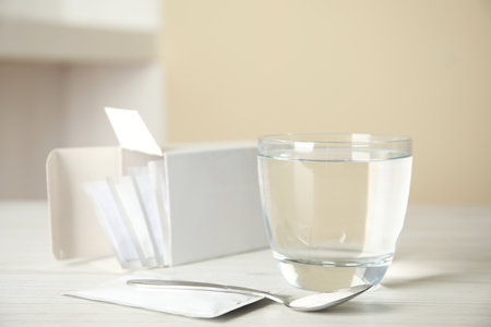 Medicine sachets, glass of water and spoon on white tableの写真素材