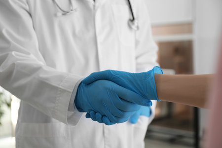Doctor and patient in protective gloves shaking hands indoors, closeupの写真素材