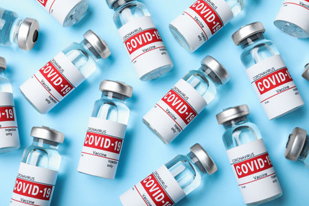 Glass vials with COVID-19 vaccine on light blue background, flat layの写真素材