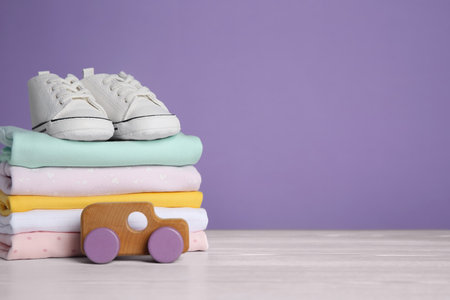 Children's shoes, stack of clothes and toy on white wooden table. Space for textの写真素材
