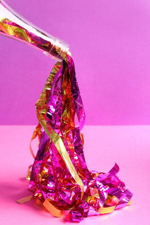 Champagne bottle with bright party streamers on pink background