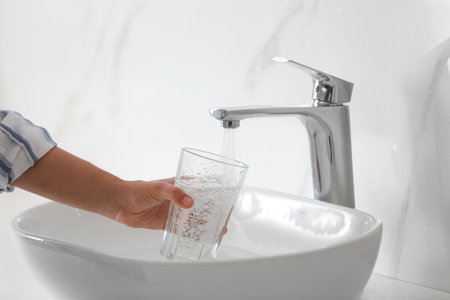 Woman filling glass with water from faucet over sink, closeupの写真素材