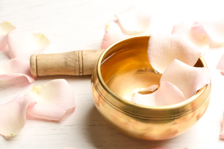 Golden singing bowl with petals and mallet on white wooden table, closeup. sound healingの写真素材