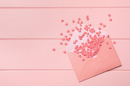 Heart shaped sprinkles with envelope on pink wooden table, flat lay. Space for textの写真素材
