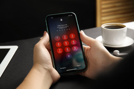MYKOLAIV, UKRAINE - JULY 9, 2020: Woman holding Iphone 11 with numpad for entering passcode on screen at black table, closeupのeditorial素材