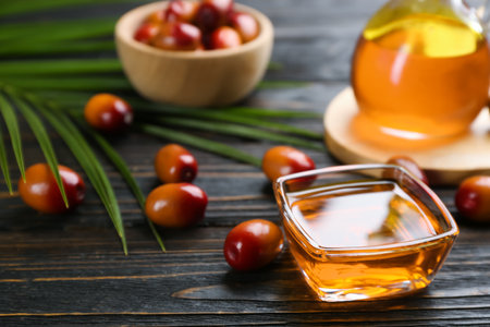 Palm oil in glass bowl, tropical leaf and fruits on wooden table. Space for textの写真素材