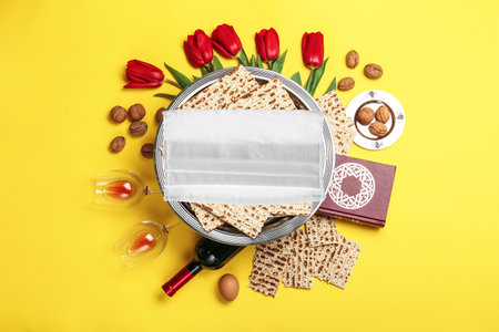 Flat lay composition with Passover matzos and protective face mask on yellow background