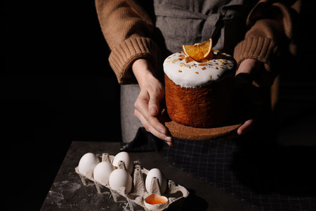 Young woman holding traditional decorated Easter cake on black background, closeup. Space for textの写真素材