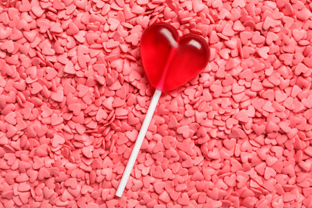 Sweet heart shaped lollipop on pink sprinkles as background, top view. Valentine's day celebrationの写真素材