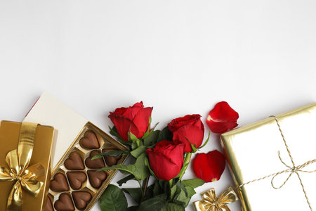 Heart shaped chocolate candies, roses and gift boxes on white background, top view. Valentine's day celebrationの写真素材