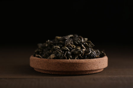 Dried green tea leaves in cork bowl on wooden table, closeup
