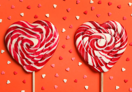Sweet heart shaped lollipops and sprinkles on coral background, flat lay. Valentine's day celebrationの写真素材