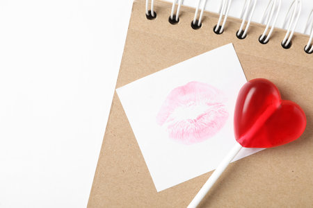Heart shaped lollipop, notebook and paper note with lipstick kiss on white background, flat lay. Valentine's day celebrationの写真素材