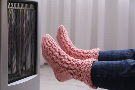 Woman warming feet near heater indoors, closeupの写真素材