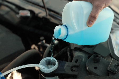 Man pouring antifreeze from plastic canister into windshield washer fluid reservoir, closeupの写真素材