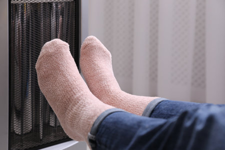 Woman warming feet near heater indoors, closeupの写真素材
