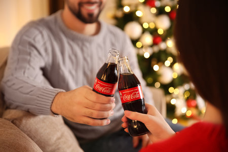 MYKOLAIV, UKRAINE - JANUARY 27, 2021: Young couple holding bottles of Coca-Cola in room decorated for Christmas, closeupのeditorial素材