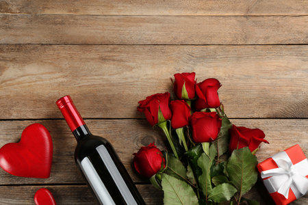 Flat lay composition with beautiful red roses and bottle of wine on wooden background, space for text. Valentine's Day celebrationの写真素材