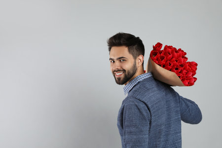 Happy man with red tulip bouquet on light gray background, space for text. 8th of March celebrationの写真素材