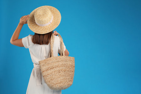 Young woman with stylish straw bag on light blue background. Space for textの写真素材