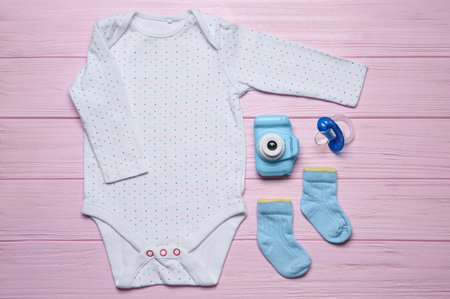 Baby clothes and camera on pink wooden background, flat layの写真素材