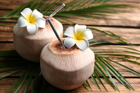 Fresh coconuts with drinking straw and flowers on wooden table, closeupの写真素材