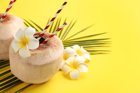 Fresh coconuts with drinking straws and flowers on yellow background. Space for textの写真素材