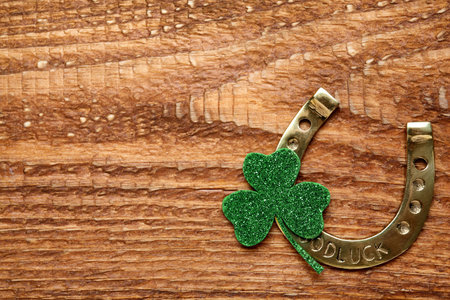 Golden horseshoe and decorative clover leaf on wooden table, flat lay with space for text. Saint...