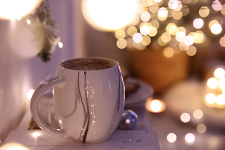 Cup of tasty hot drink against blurred Christmas lights. Space for textの写真素材