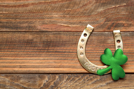 Golden horseshoe and decorative clover leaf on wooden table, flat lay with space for text. Saint Patrick's Day celebrationの写真素材