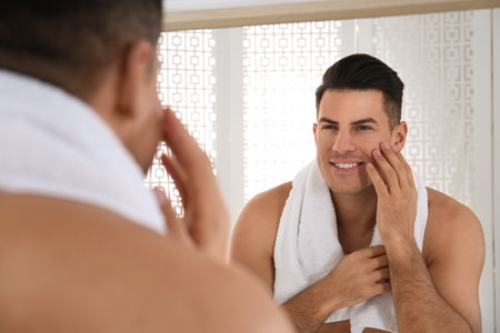 Handsome man with towel near mirror in bathroomの写真素材