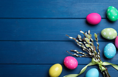 Bright painted eggs and pussy willows on blue wooden table, flat lay with space for text. happy...