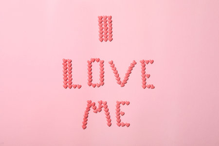 Phrase I Love Me made of heart shaped sprinkles on pink background, flat layの写真素材