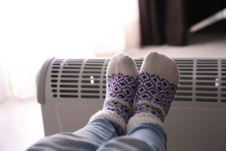 Child warming feet on electric heater at home, closeupの写真素材