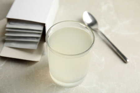 Medicine sachets, glass of water and spoon on light tableの写真素材