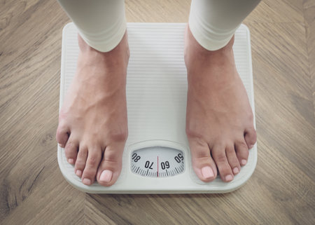 Woman using scale on floor, closeup. Overweight problem after New Year partyの写真素材