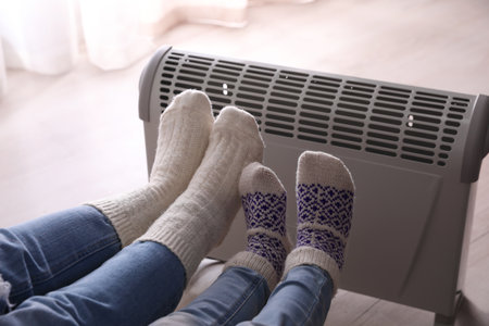 Mother and child warming feet near electric heater at home, closeupの写真素材