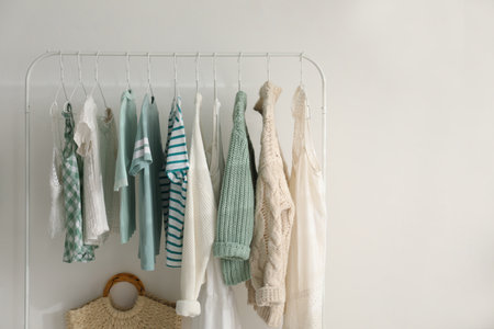 Rack with stylish women's clothes near white wall, space for text. interior design