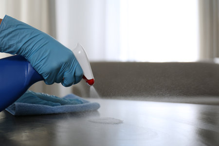 Woman in gloves cleaning gray stone table with rag and detergent indoors, closeup. Space for textの写真素材
