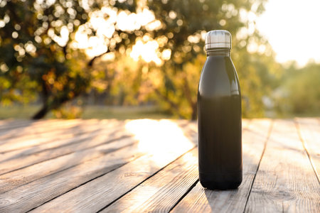 Modern black thermo bottle on wooden surface outdoors. Space for textの写真素材