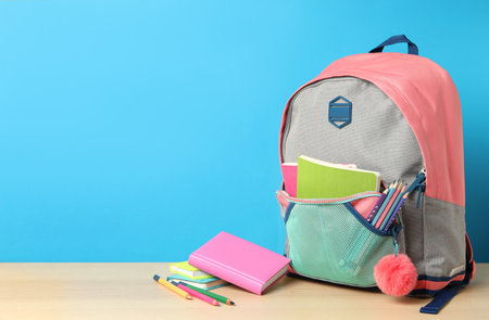 Stylish backpack and different school stationery on wooden table against light blue background, space for text. back to schoolの写真素材