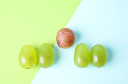 Row of green grapes and pink one on color background, flat lay. uniqueness conceptの写真素材
