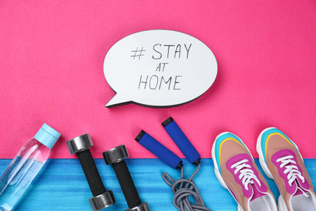 Sport equipment and speech bubble with hashtag STAY AT HOME on colorful yoga mats, flat lay.の写真素材