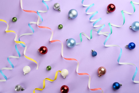 Colorful serpentine streamers and Christmas balls on violet background, flat layの写真素材