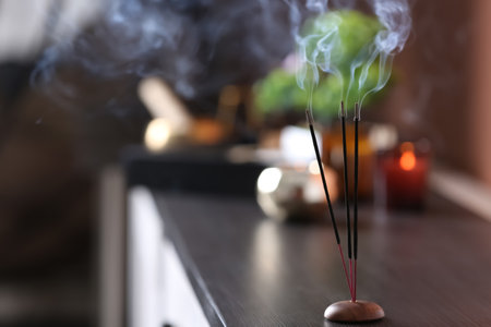 Incense sticks smoldering on wooden chest of drawers in room. Space for textの写真素材
