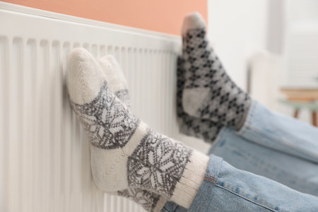 Couple warming legs on heating radiator indoors, closeupの写真素材