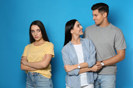 Unhappy woman feeling jealous while couple spending time together on blue backgroundの写真素材