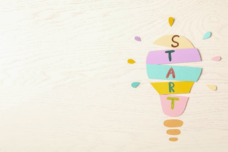Lightbulb with word Start made of paper sheets on white wooden background, flat lay. Space for text