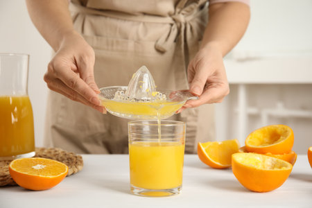Woman pouring freshly made orange juice in glass at white table, closeupの写真素材