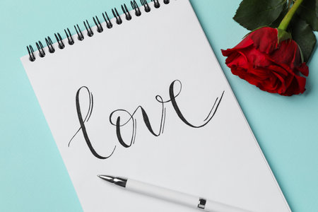Notepad with handwritten word LOVE and rose on turquoise background, flat layの写真素材